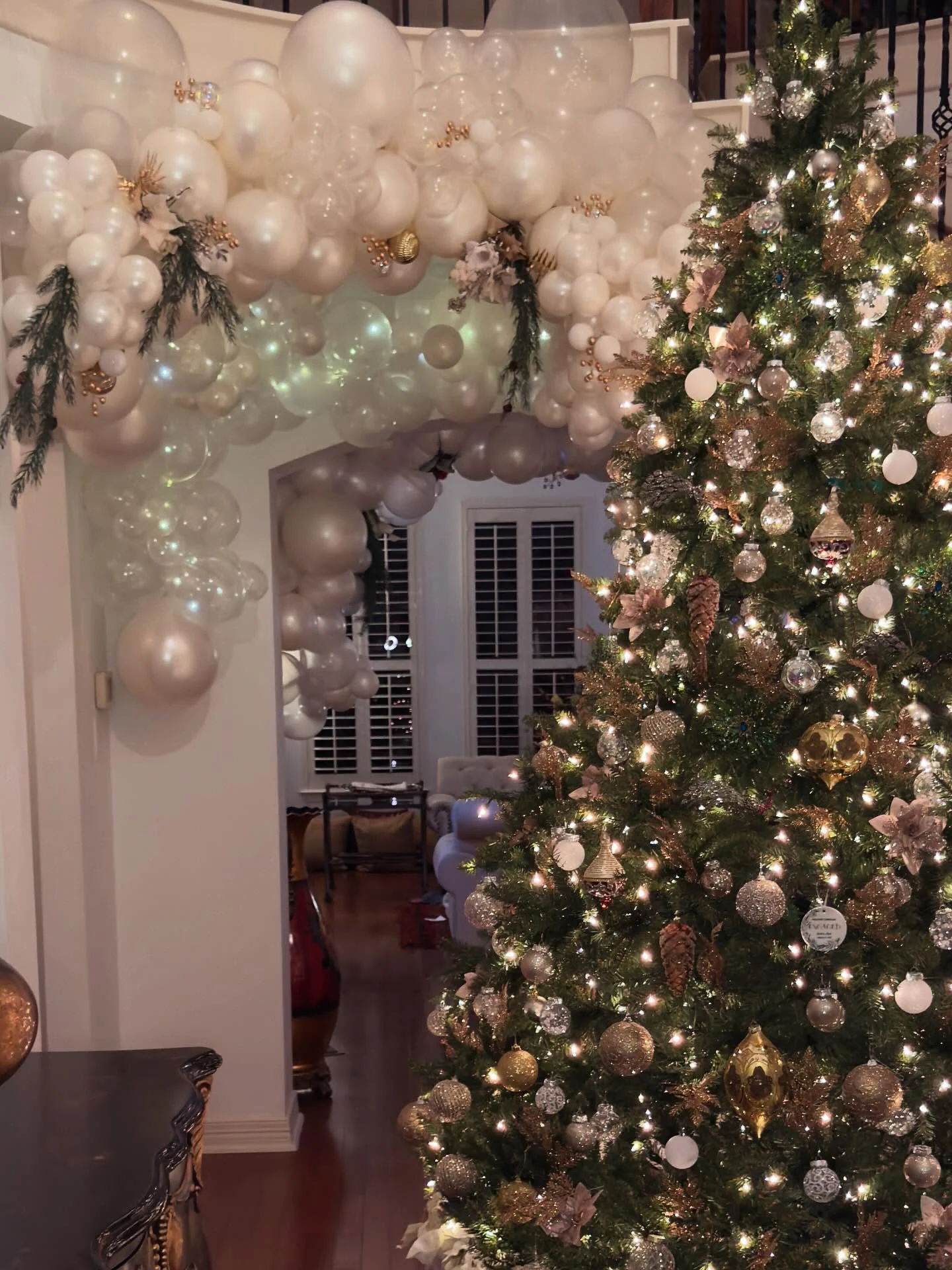Pearl and ivory balloon garland framing a doorway beside a decorated holiday tree.