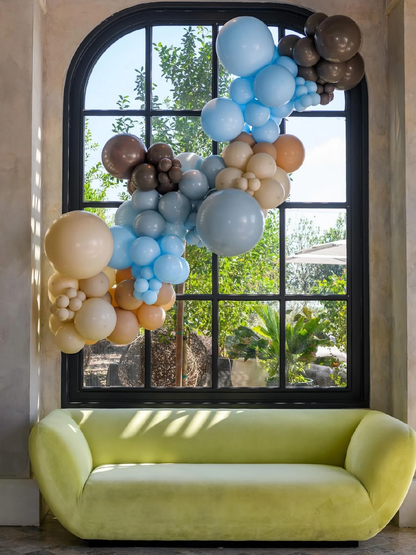 Blue, ivory and taupe balloon garland across an arched window above a green sofa.