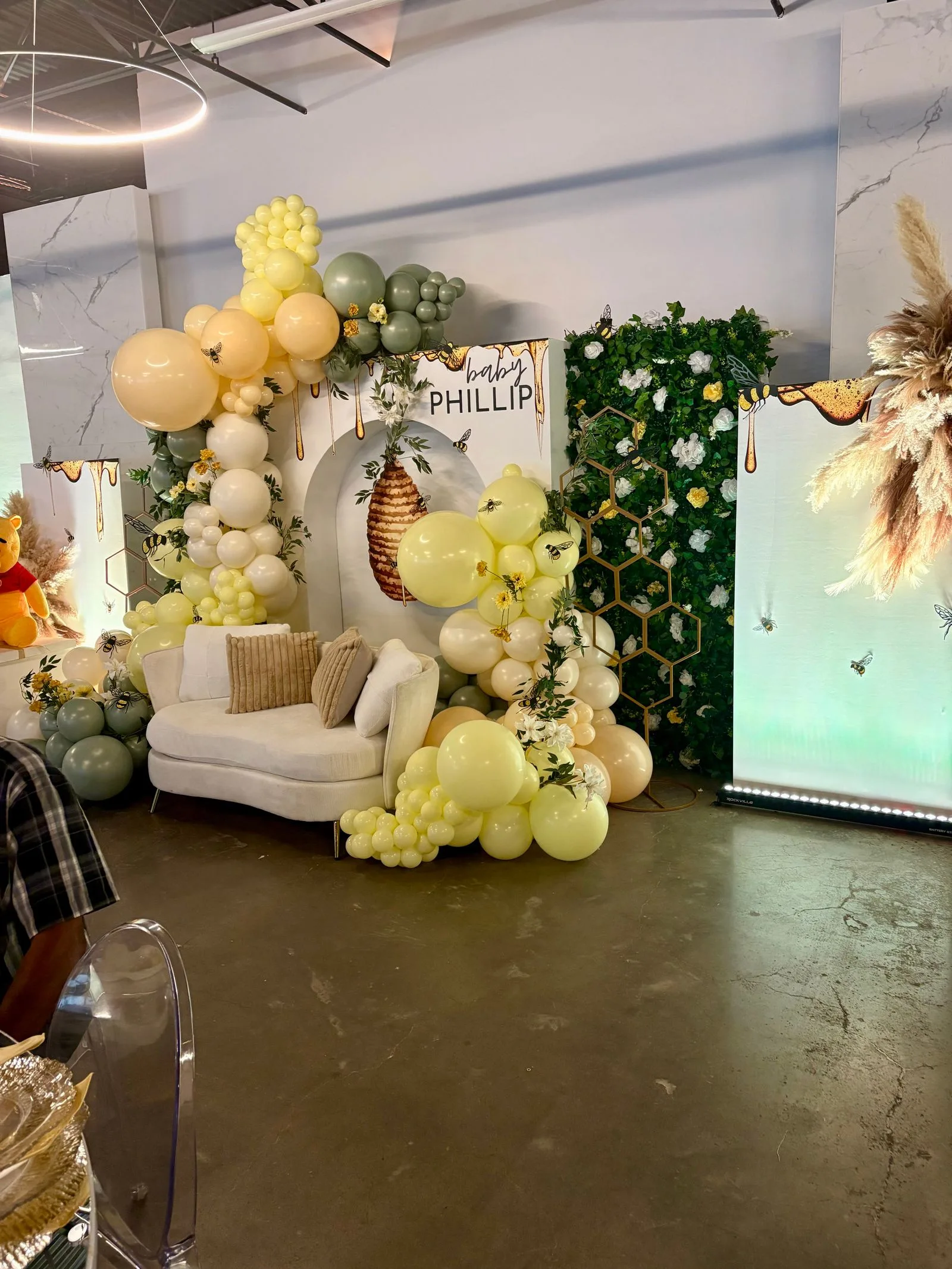 Yellow, cream and sage balloons frame a honey-themed backdrop with a small sofa and greenery.