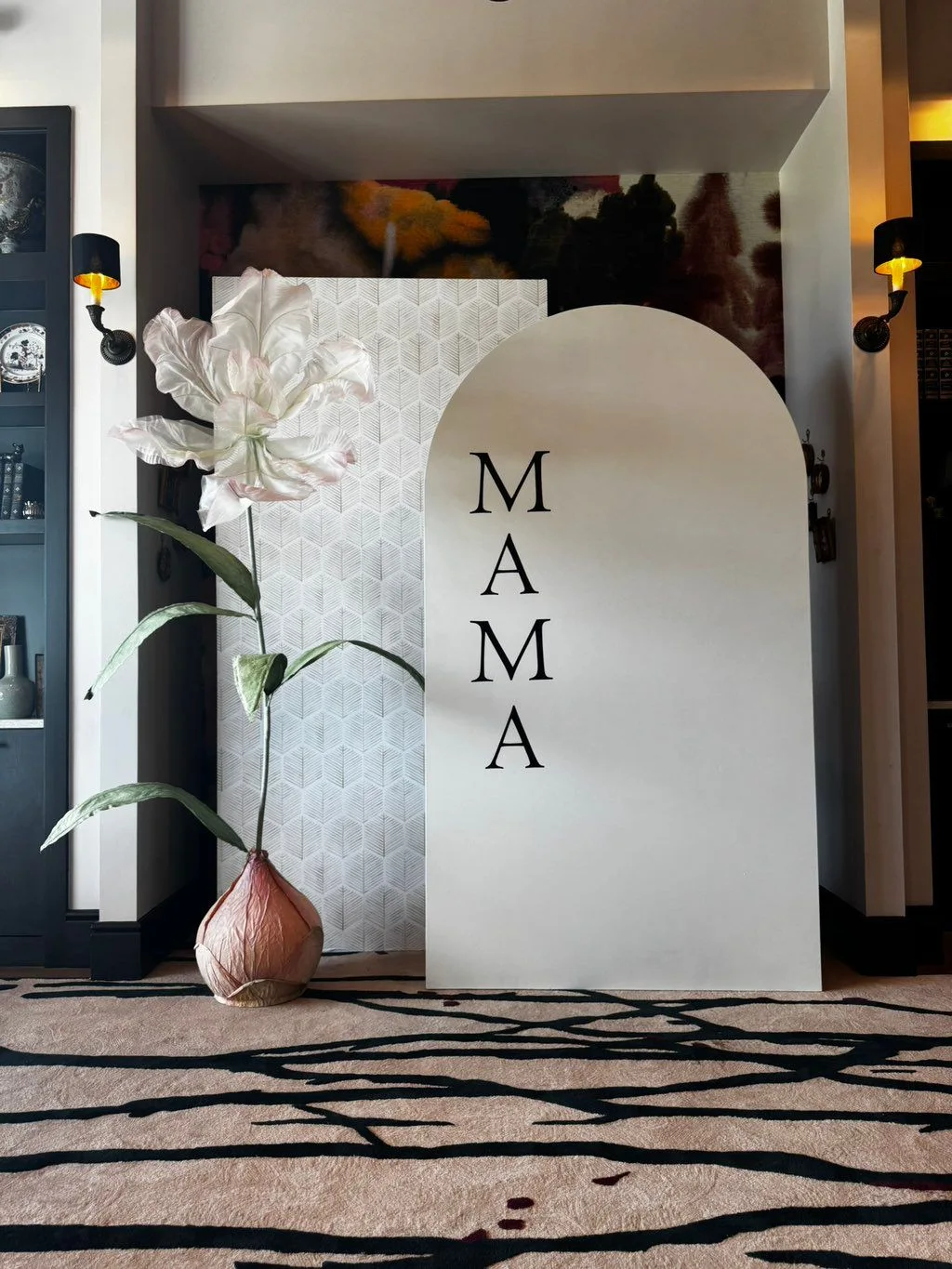 A white textured backdrop and arched MAMA panel sit beside an oversized sculptural flower.