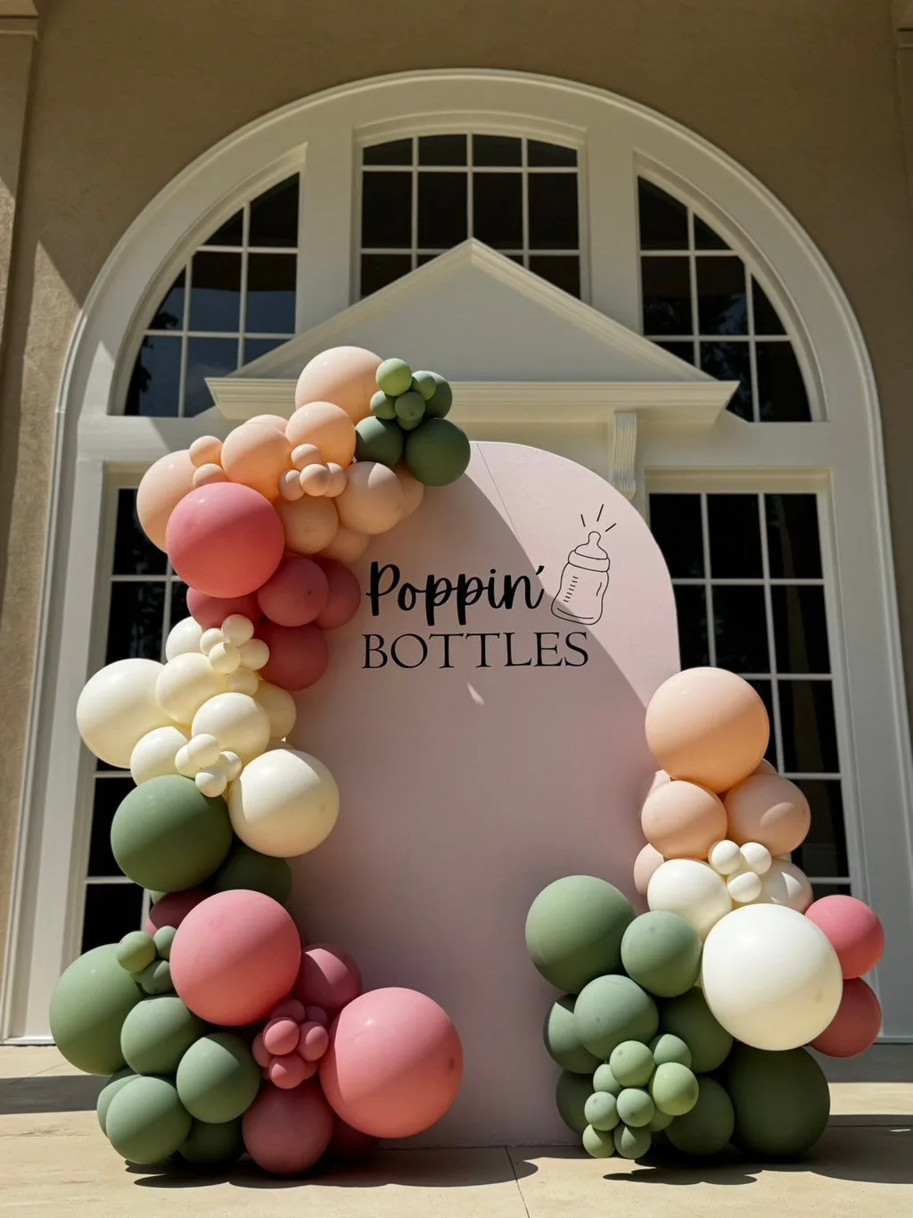 Pastel pink, peach, sage and cream balloons surround a Poppin' Bottles baby-shower backdrop.