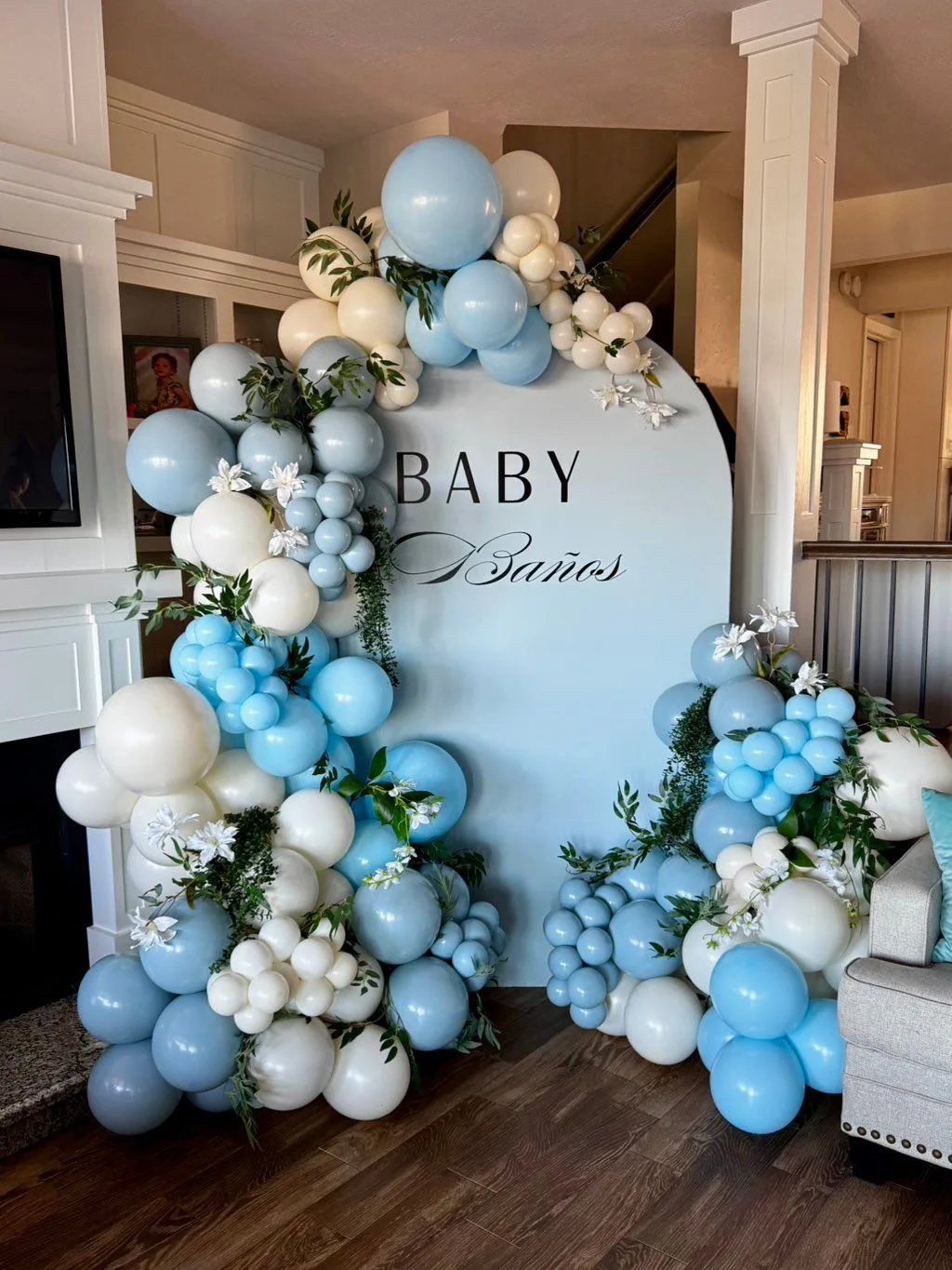 Blue and ivory balloons with white flowers and greenery frame a baby-shower backdrop.